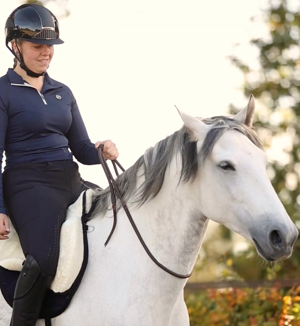 Woman riding a white horse bridleless with a bareback pad and bridleless neck rope
