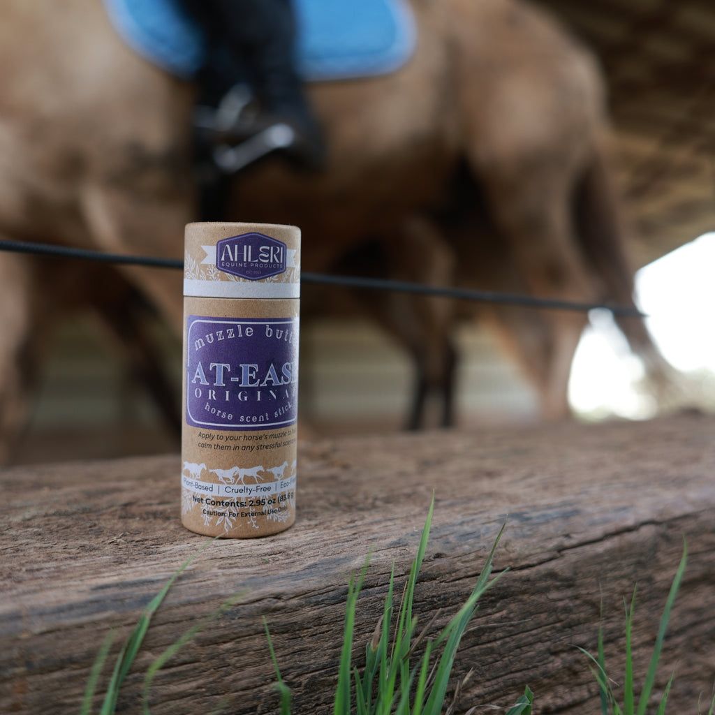 Ahleri Muzzle Butter: At-Ease horse scent stick sitting on riding arena fence with horses in the bakcground.